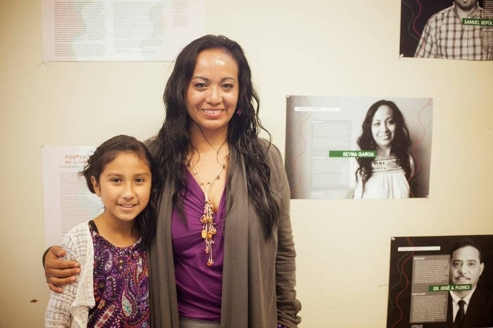 Woman and child standing in front of a portrait of the woman